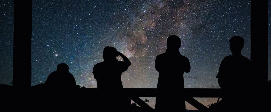 Four people stargazing silhouetted against the milky way