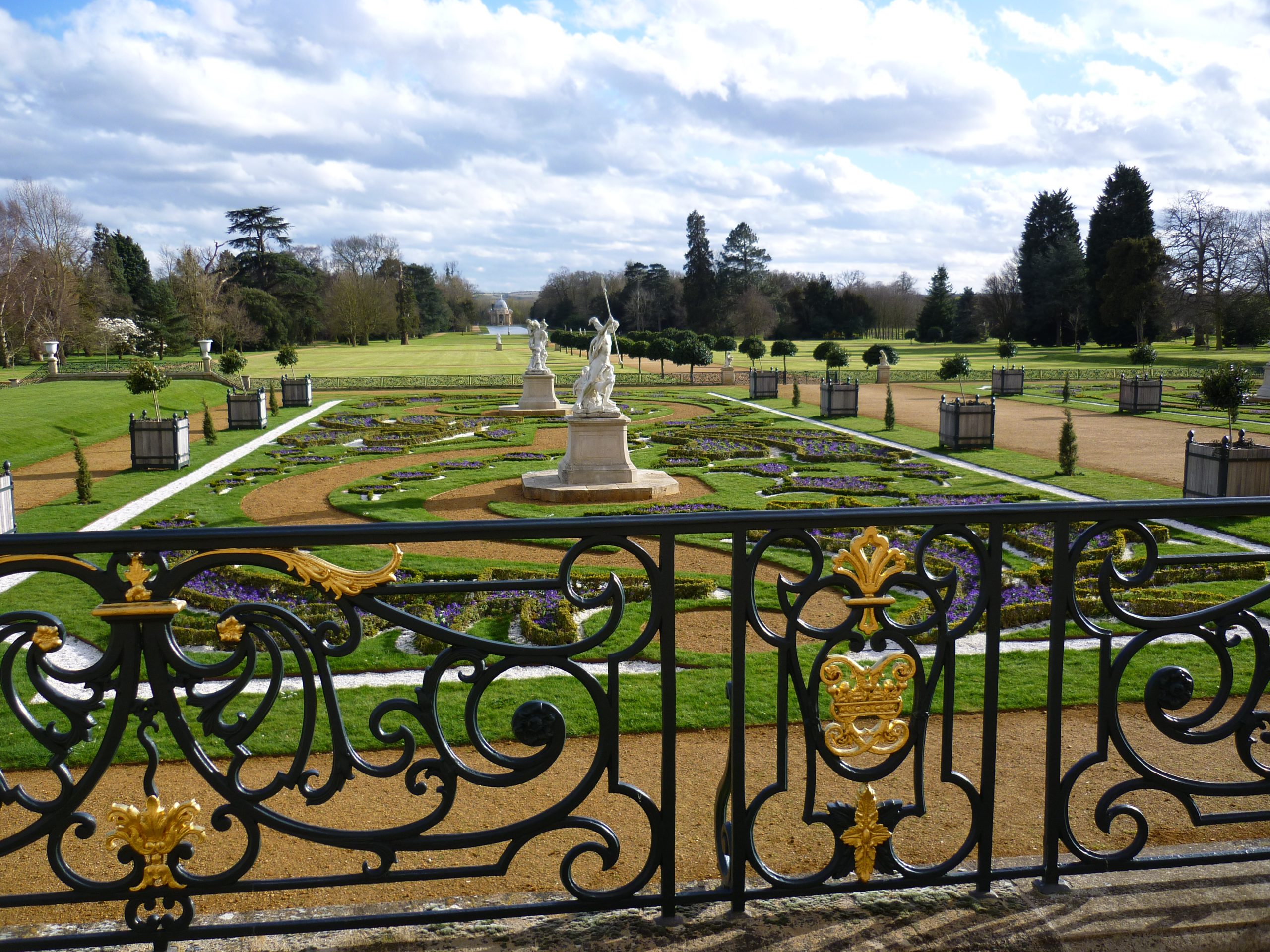 View of a parterre and formal gardens through ornate black railings.