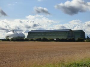 A large hangar with airship outside, seen from across a field.