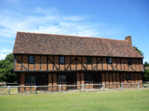 A red brick and timber framed hall, fronted by a green.