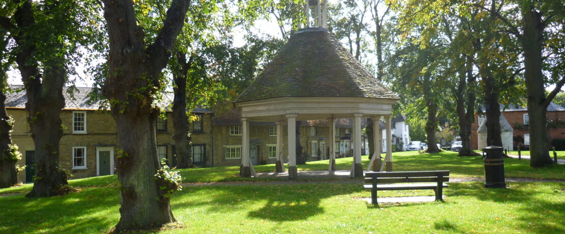 An open octagonal building on a village green.