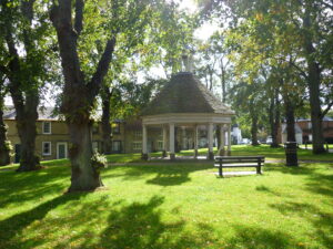 An open octagonal building on a village green.