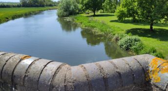 A wide calm river, lined with greenery, seen from a bridge.