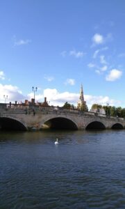 Bridge over a river on a sunny day, with church spire in the background.
